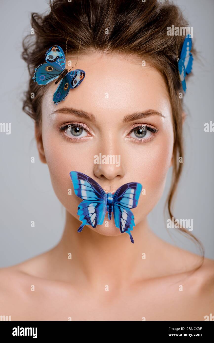 bella giovane donna con farfalle decorative sul viso isolato su grigio Foto Stock