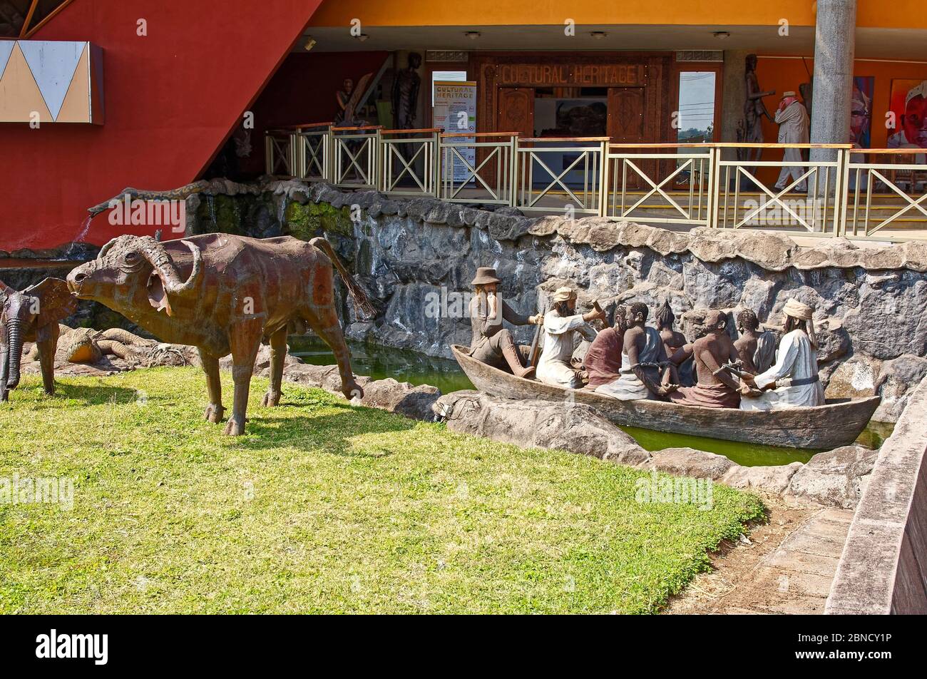 Sculture all'aperto, canoa che trasporta schiavi legati, capitori, animali selvatici, arte, erba, edificio, Centro Culturale, Africa, Arusha, Tanzania Foto Stock