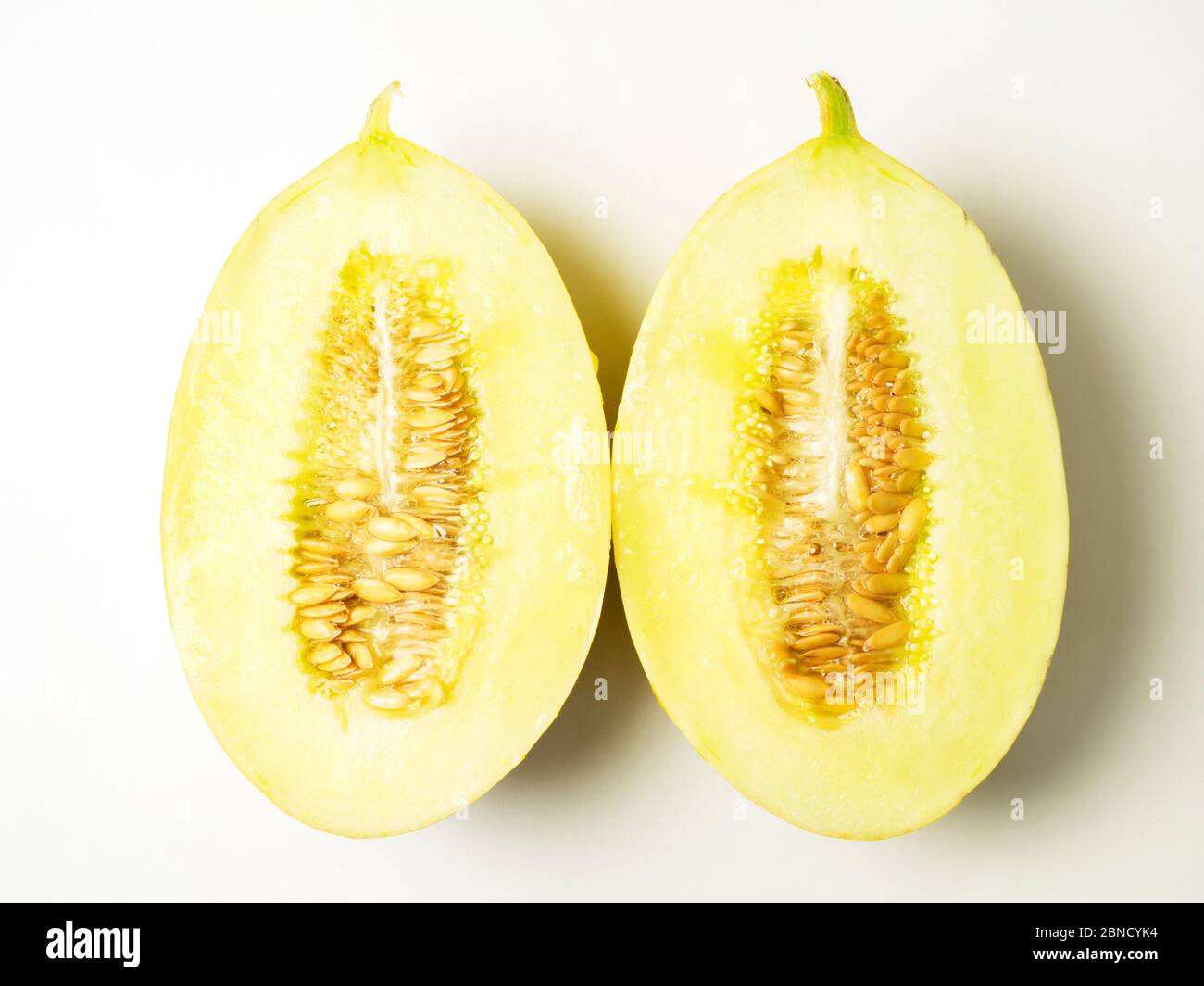 Due metà di un melone canarino con semi su sfondo bianco Foto Stock