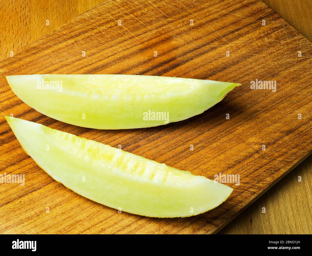 Due fette di melone canarino su una tagliere di legno Foto Stock