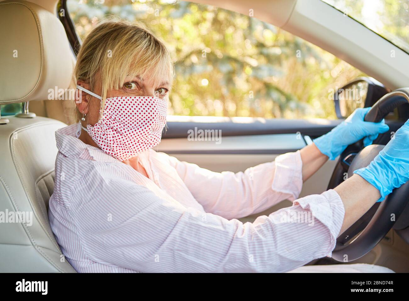 Donna anziana con maschera facciale e guanti monouso a causa di pandemia di coronavirus al volante della sua auto Foto Stock