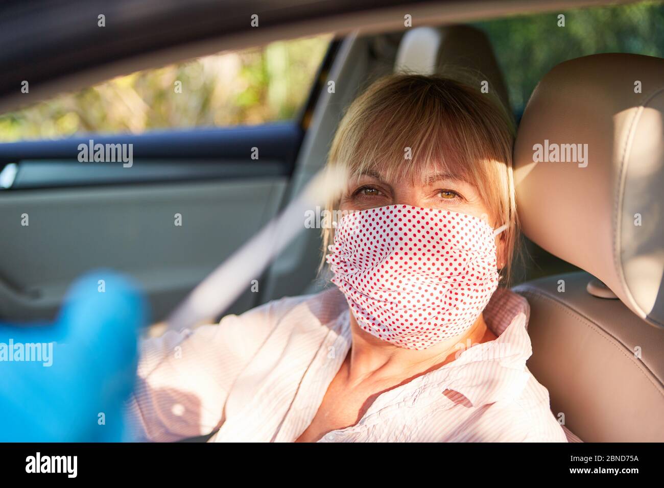 La donna anziana con maschera facciale nella sua auto si muove per un test rapido durante la pandemia del coronavirus Foto Stock