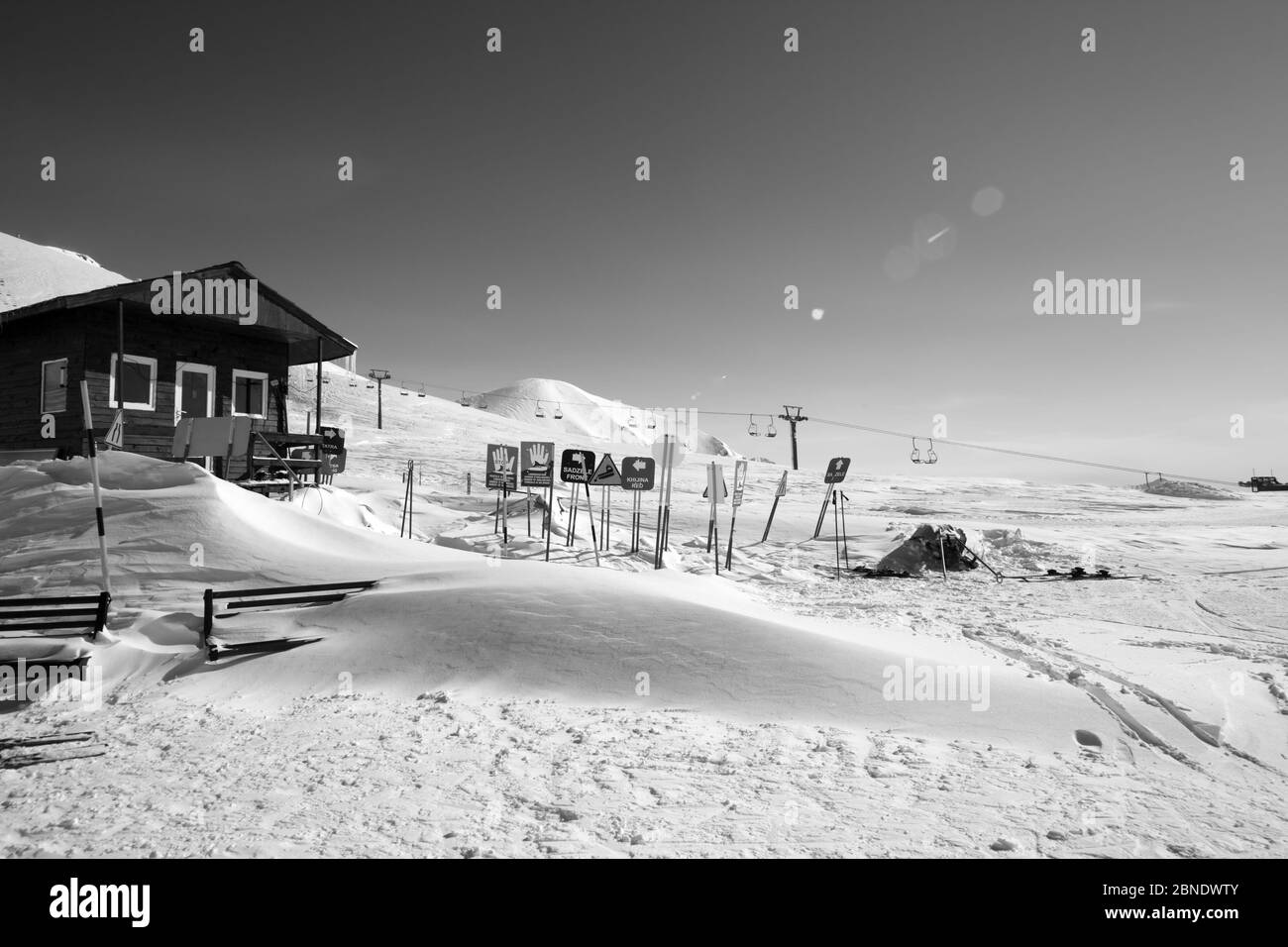 Montagne innevate bianche e nere, casa di salvataggio in legno, cartelli di allarme in motoslitta, seggiovia e cielo limpido con fascio solare. Montagne del Caucaso al sole Foto Stock