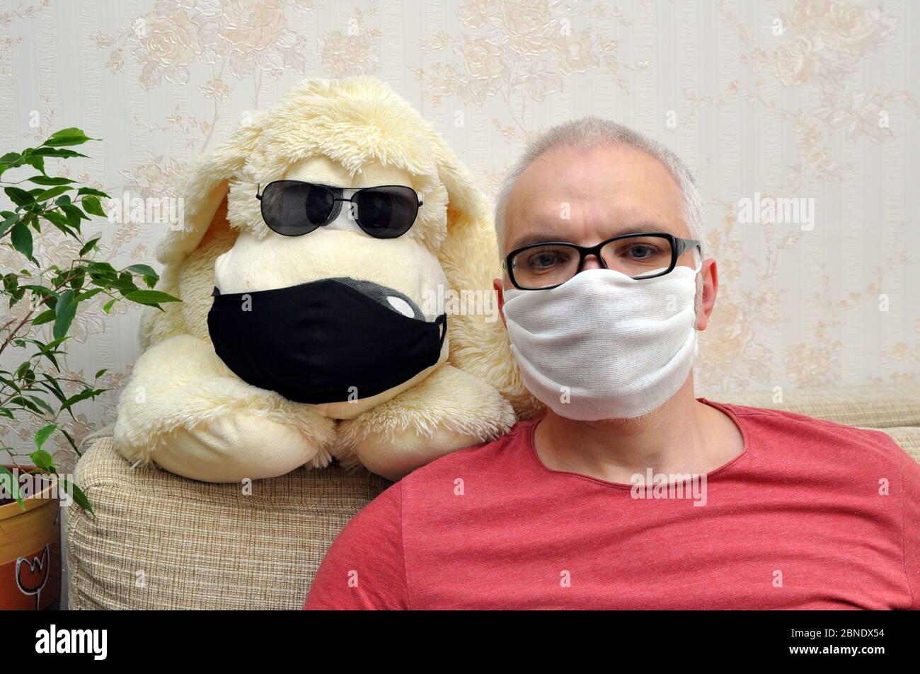 Un uomo in una maschera medica con un cane giocattolo è a casa isolato. Concetto di prevenzione del coronavirus Foto Stock