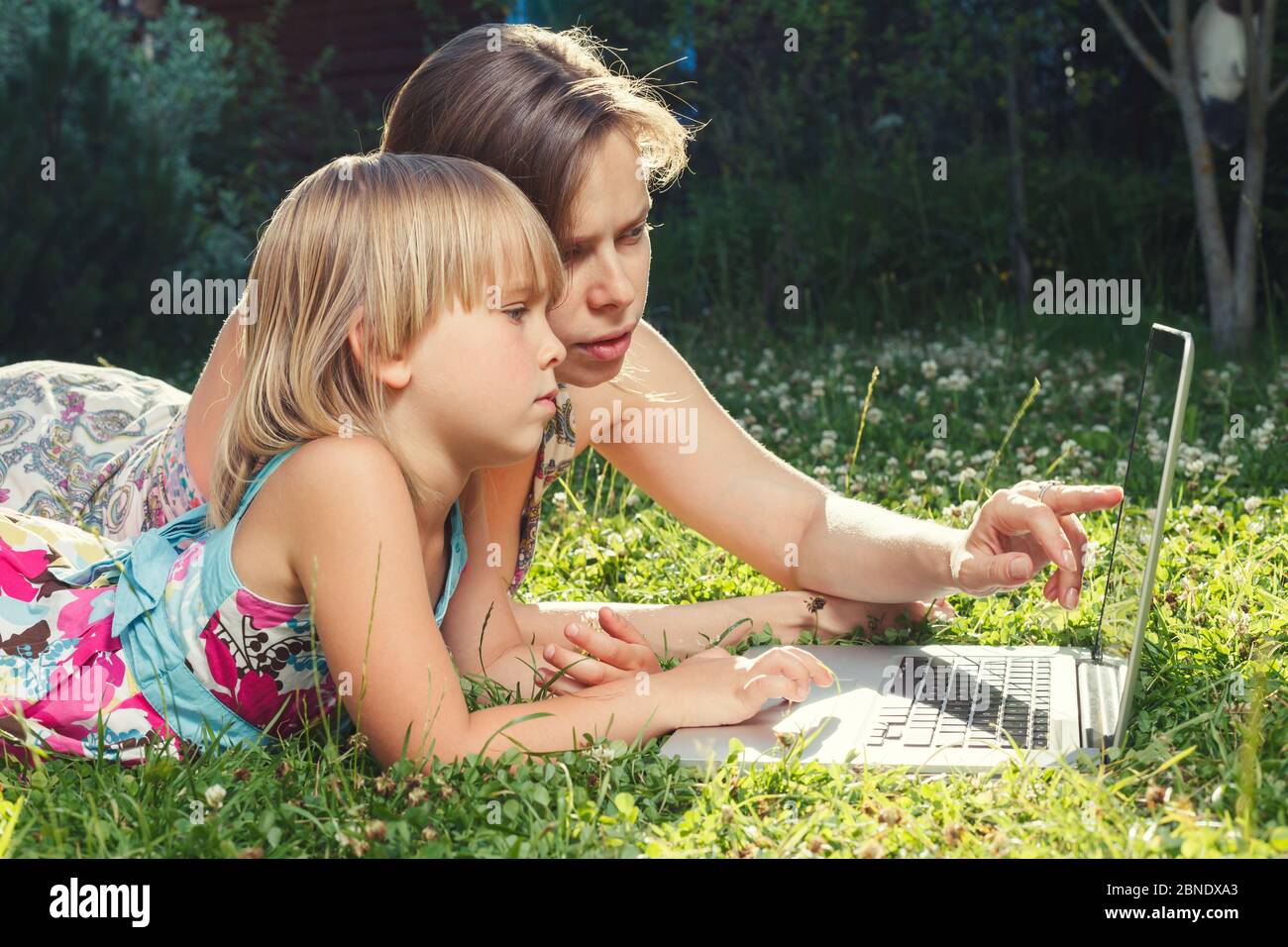 Madre che aiuta la sua piccola figlia a utilizzare il computer portatile. Bambino che studia a casa facendo il suo lavoro o avendo lezione in linea. Concetto di homeschooling Foto Stock