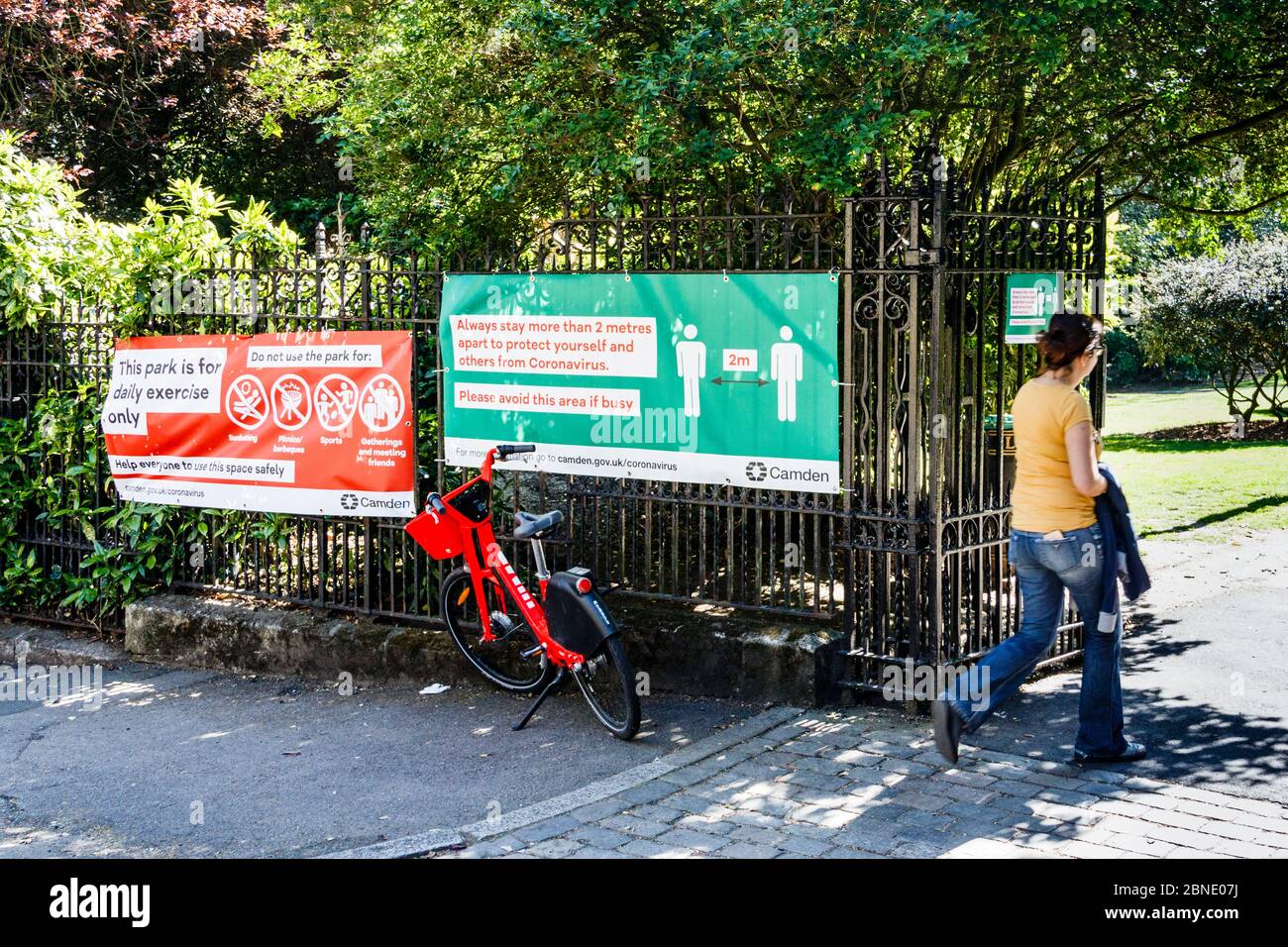 Una donna che entra in un parco per l'esercizio in una giornata di sole durante il blocco pandemico del coronavirus, consigli su allontanamento sociale alle porte, Londra, Regno Unito Foto Stock