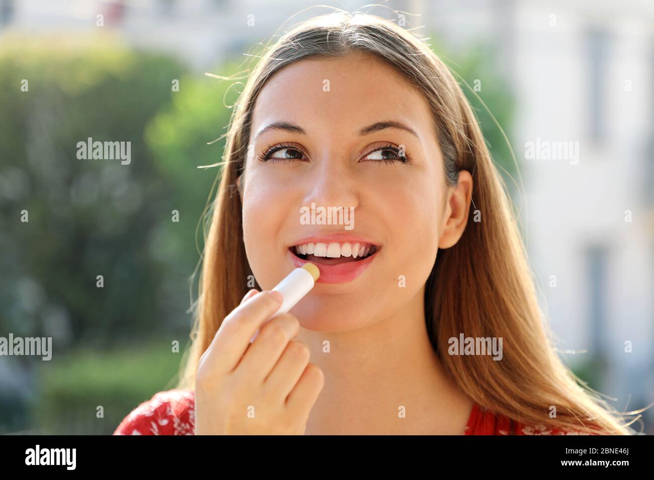 Ritratto di una giovane donna felice che applica balsamo labbro in estate all'aperto Foto Stock