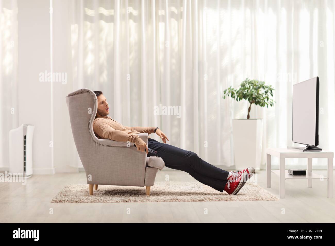 Un giovane che dorme in una poltrona davanti alla tv di casa Foto Stock