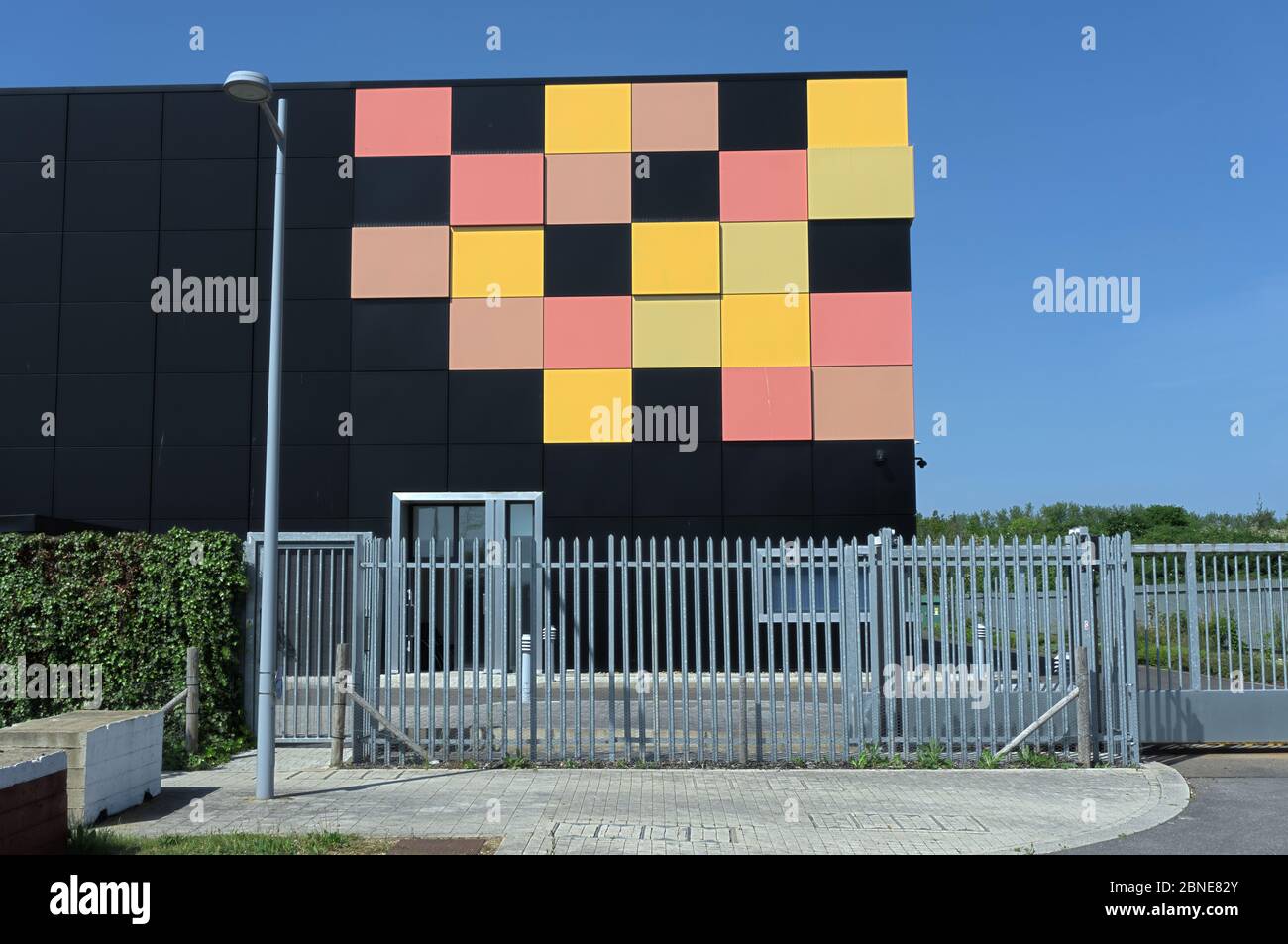 Edificio cubico nero opaco con piastrelle gialle e rosse in un angolo come design grafico dietro le ringhiere di sicurezza in metallo, data center cielo blu intenso Foto Stock