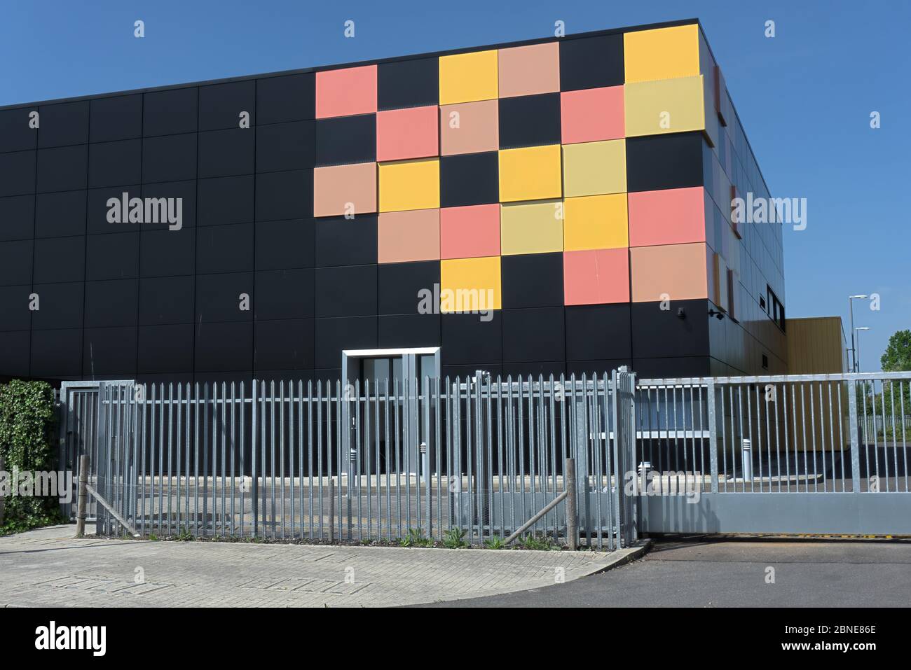 Edificio cubico nero opaco con piastrelle gialle e rosse in un angolo come design grafico dietro le ringhiere di sicurezza in metallo, data center cielo blu intenso Foto Stock