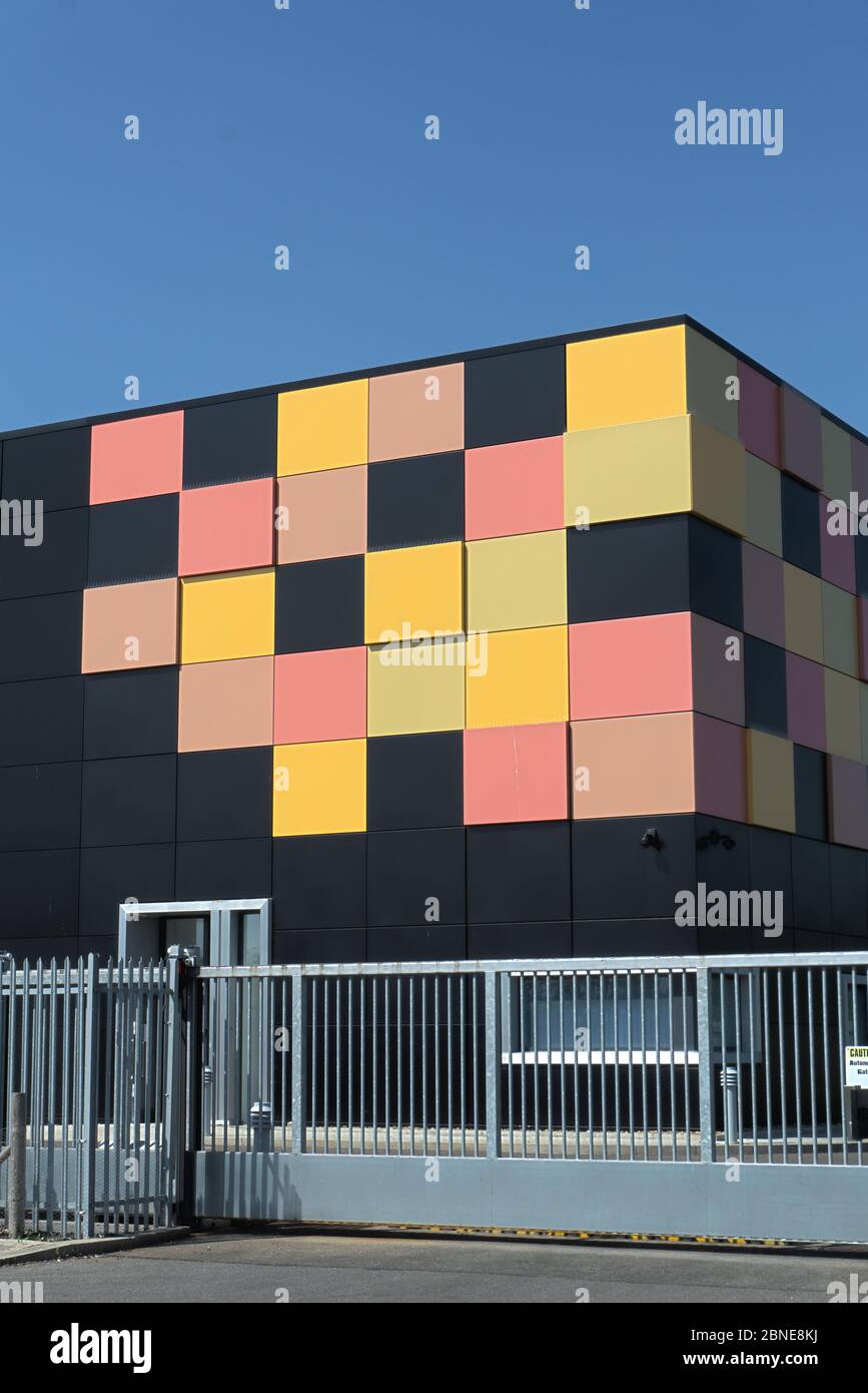 Edificio cubico nero opaco con piastrelle gialle e rosse in un angolo come design grafico dietro le ringhiere di sicurezza in metallo, data center cielo blu intenso Foto Stock