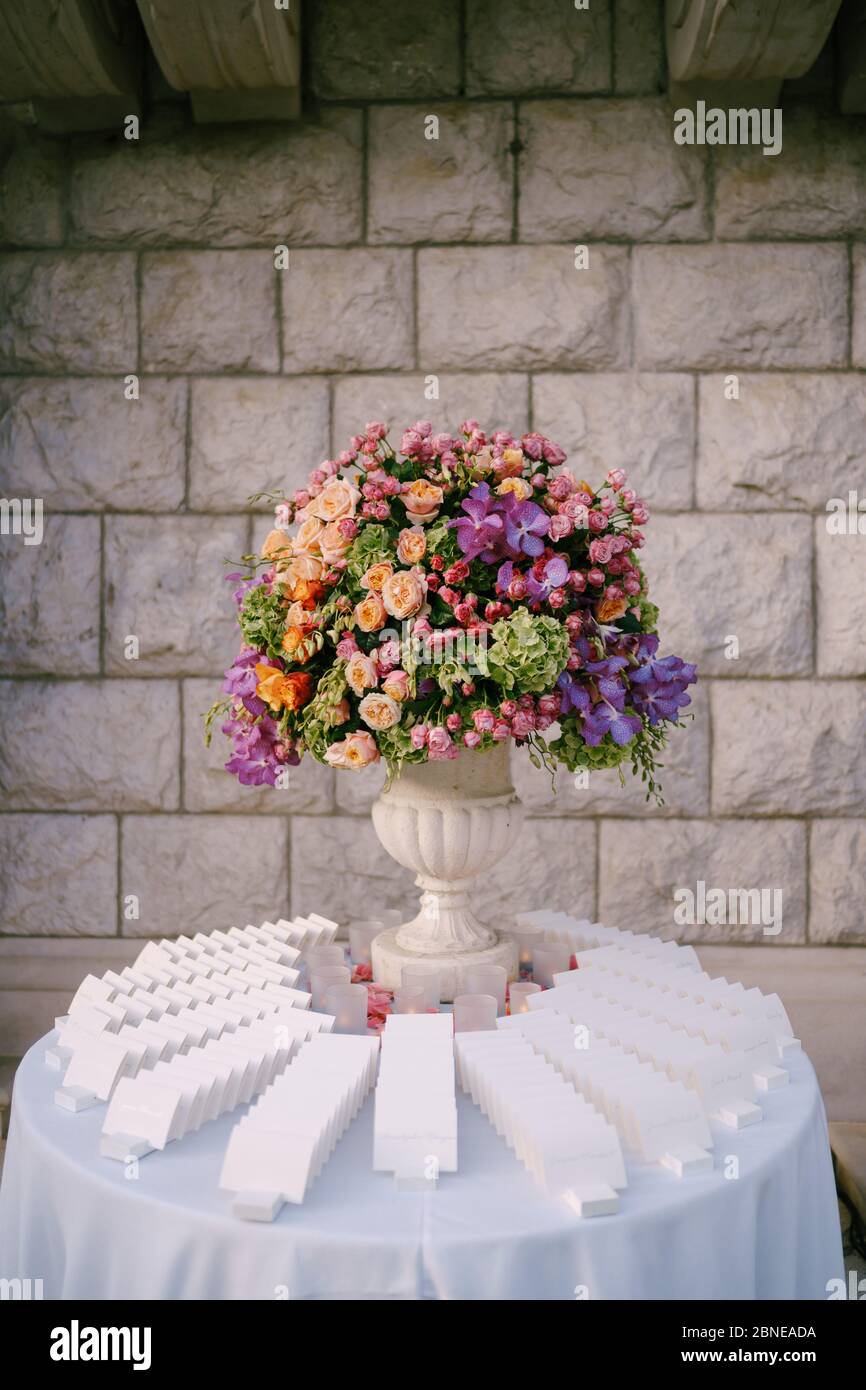 Ricevimento con tavolo da pranzo per matrimoni. Un bouquet enorme in un antico vaso di marmo di rose rosa, rosse, arancioni e gialle, idrangee verdi, orchidee viola. Stand Foto Stock