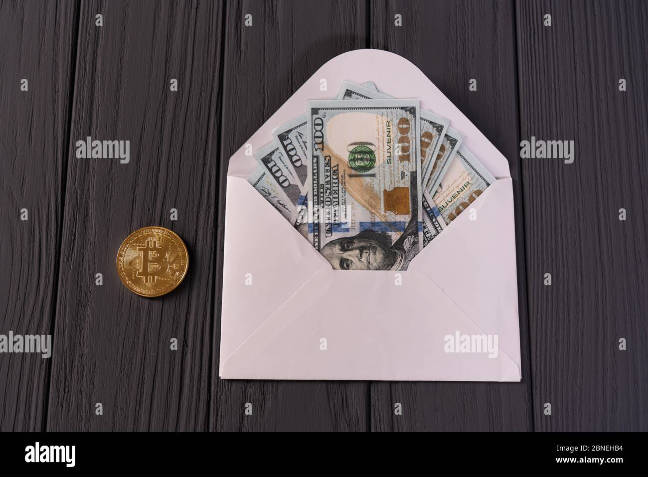 Una busta con dollari e bitcoin isolato su sfondo grigio di legno Foto Stock