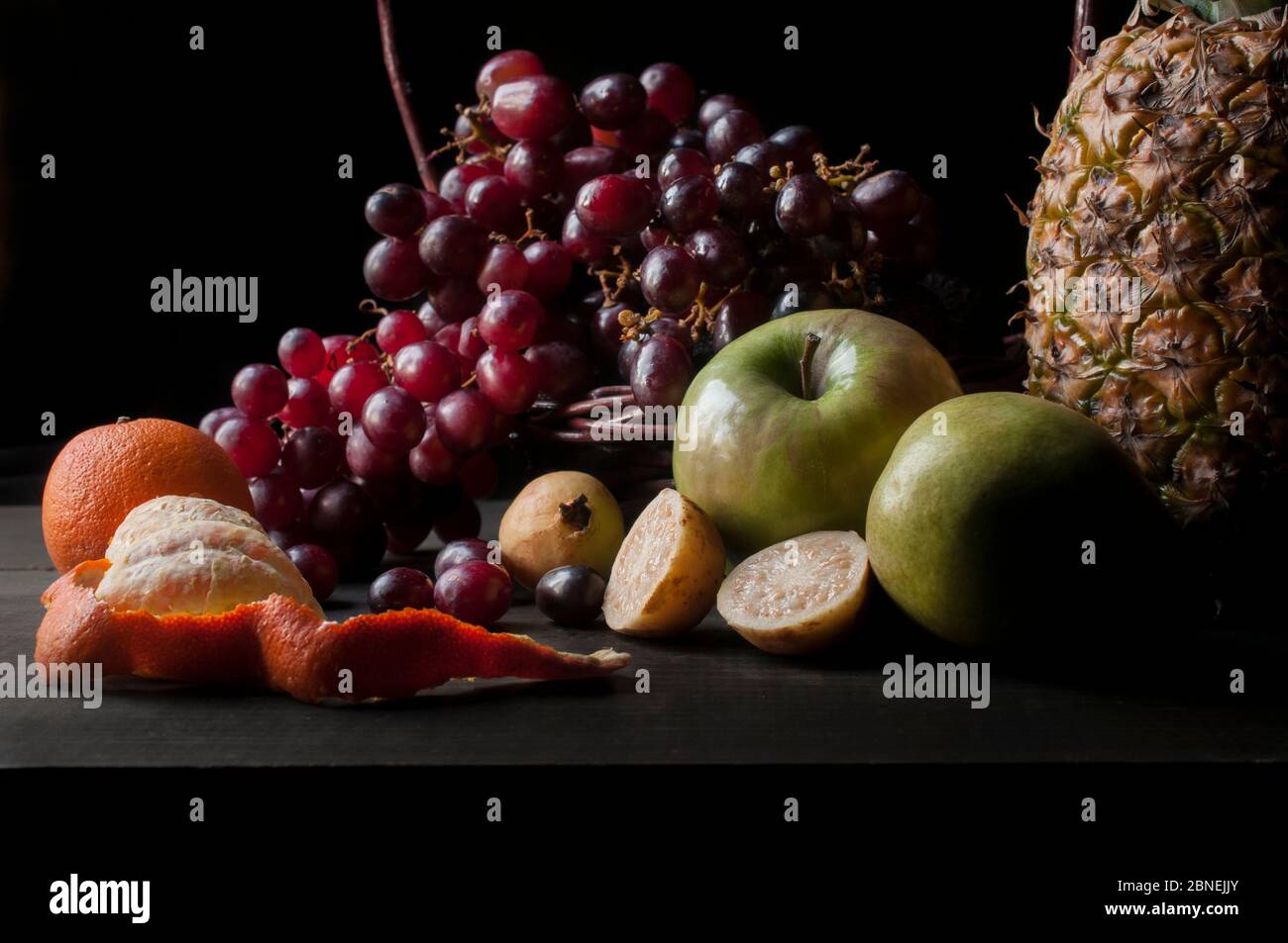 Fotografia rinascimentale o chiaroscuro di fotografia di frutta morta con uva, ananas, mele verdi, guava, mandarino e uva rossa Foto Stock