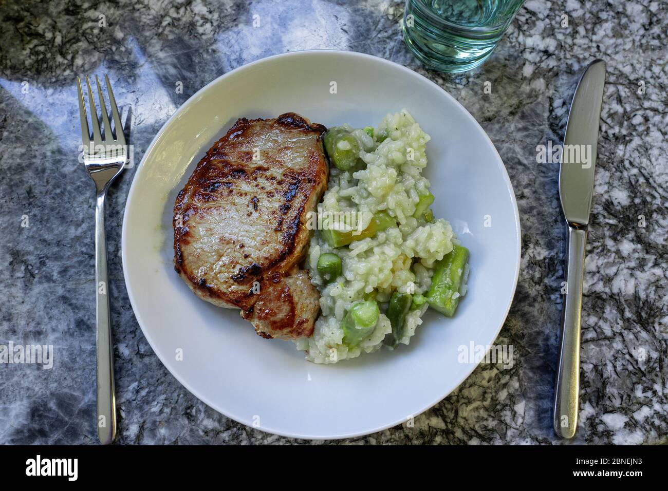 Carne arrosto e risotto con asparagi in piatto bianco rotondo con forchetta e coltello su fondo di granito. Vista ad angolo alto. Foto Stock