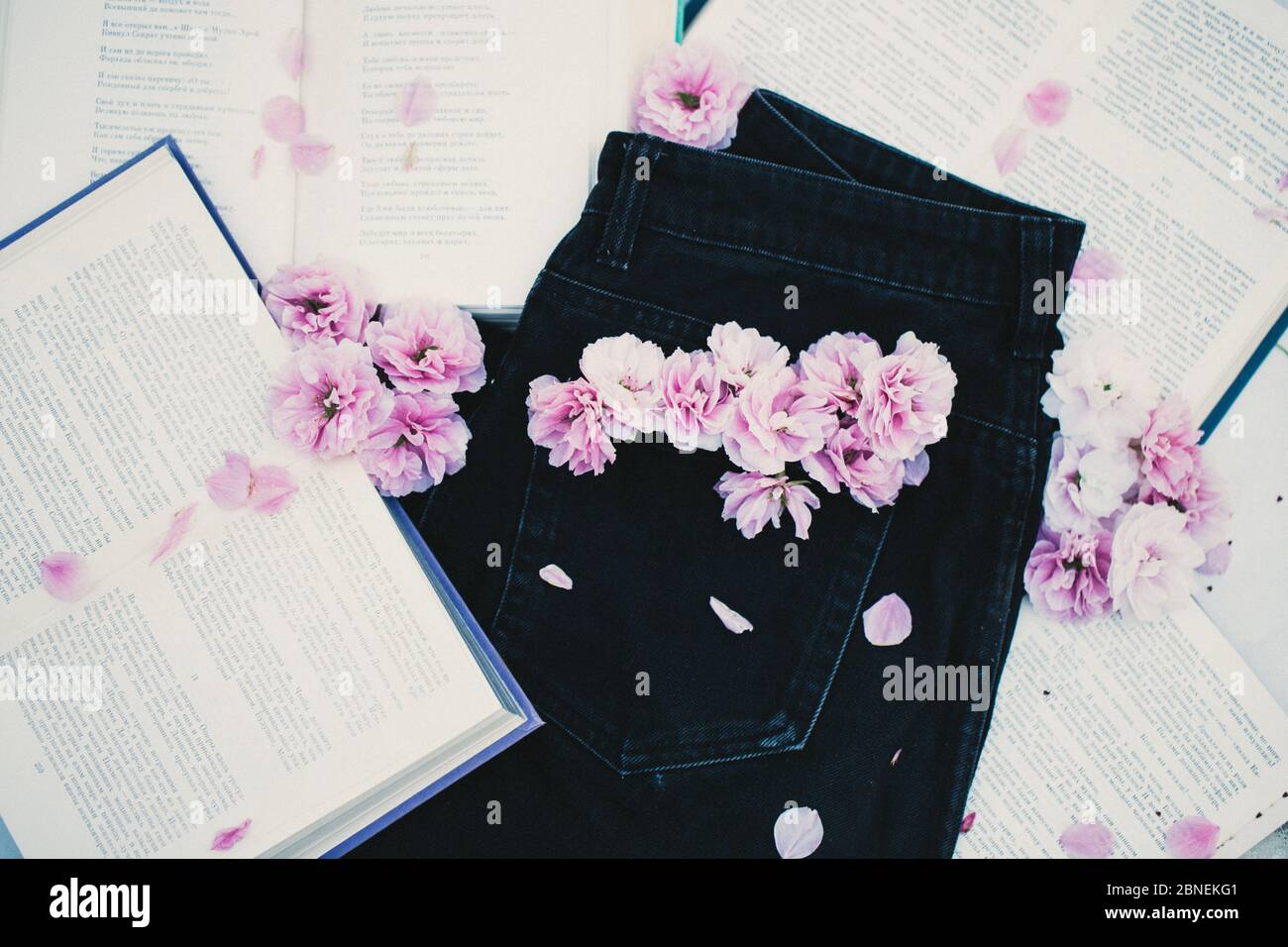 Jeans neri con fiori sakura nella tasca posteriore e libri intorno ad esso romantico hipster umore Foto Stock