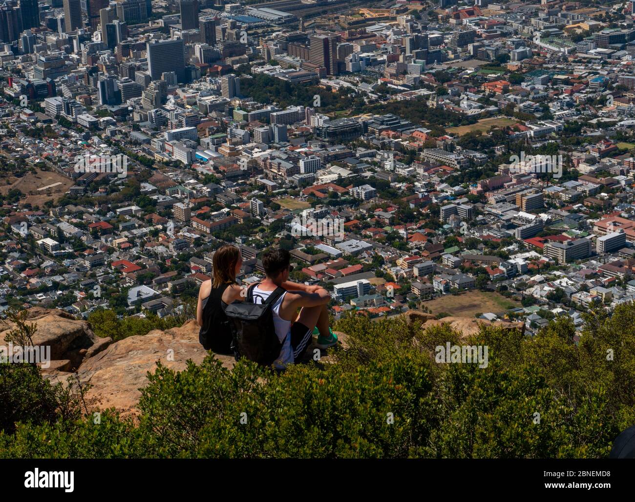 Cape Town, Sudafrica - 17 marzo 2020:giovane coppia seduta sulla roccia sulla cima della montagna testa del Leone guarda il paesaggio urbano di Città del Capo. Foto Stock