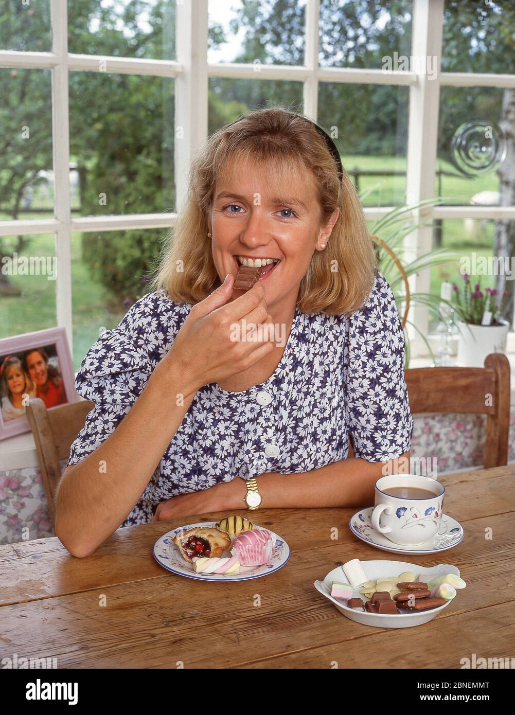 Giovane donna con una tazza di tè con torte e dolci, Winkfield, Berkshire, Inghilterra, Regno Unito Foto Stock