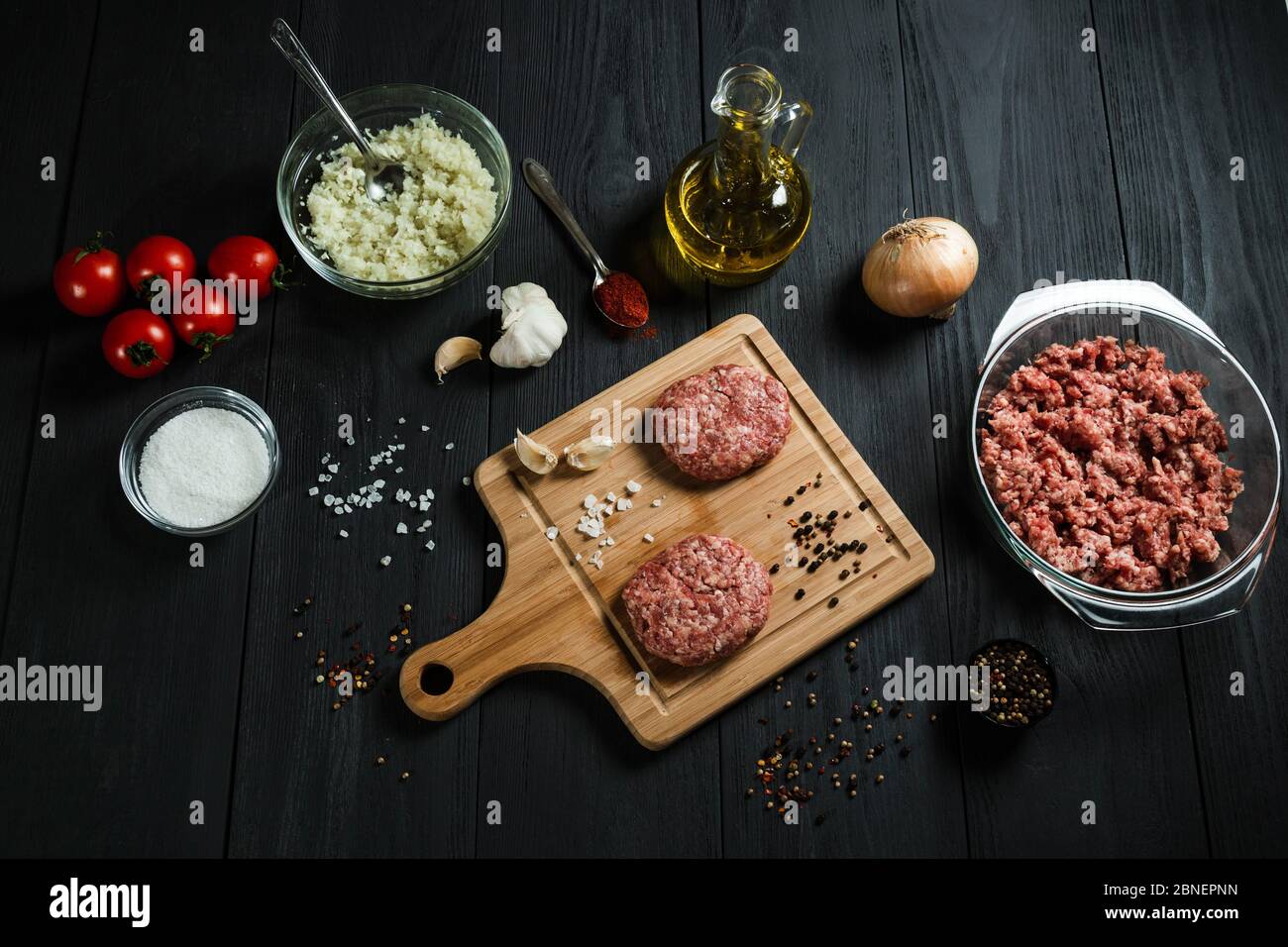 Cutlets di carne macinata con gli ingredienti sul tavolo di legno nero. Cucina casalinga. Foto Stock