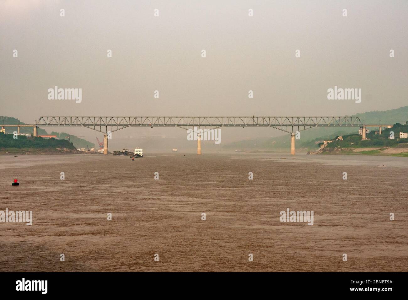 Chongqing, Cina - 8 maggio 2010: Fiume Yangtze. Ponte ferroviario in metallo grigio sull'acqua marrone sotto il cielo stollato con le coste verdi su entrambi i lati. Qualche barca Foto Stock