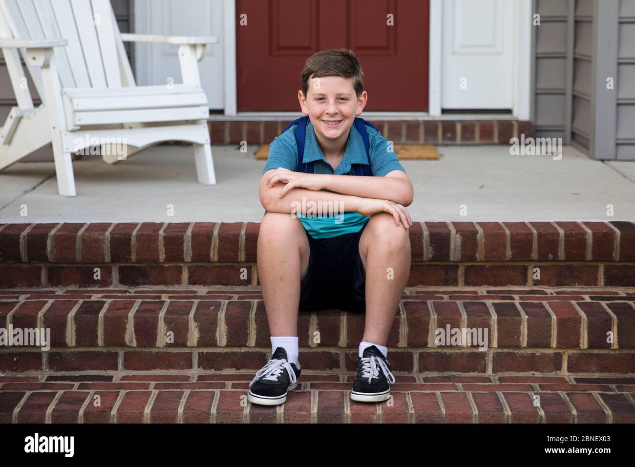 Happy Tween Boy si siede sui gradini Brick Front Foto Stock