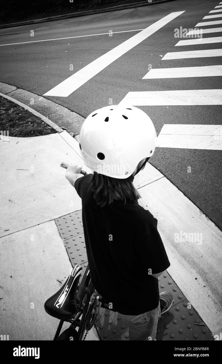 Immagine verticale in scala di grigi di un bambino che indossa un casco con una bicicletta in piedi per la strada Foto Stock