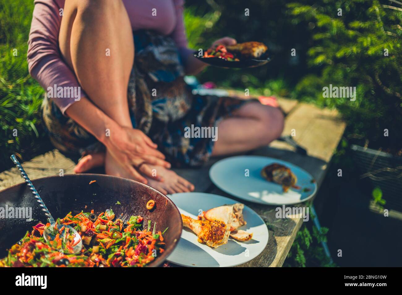 Una giovane donna sta diving insalata e pollo all'aperto in un giardino in una giornata di primavera soleggiata Foto Stock