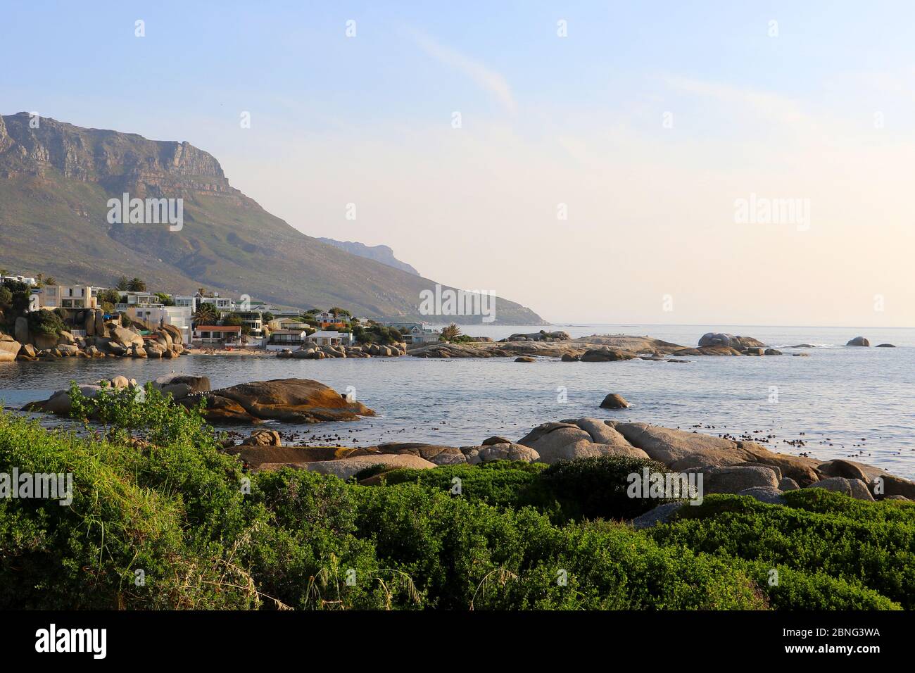 Proprietà e spiagge a Camps Bay, Città del Capo, Sud Africa in una giornata estiva limpida, con persone sulla spiaggia e le montagne sullo sfondo Foto Stock