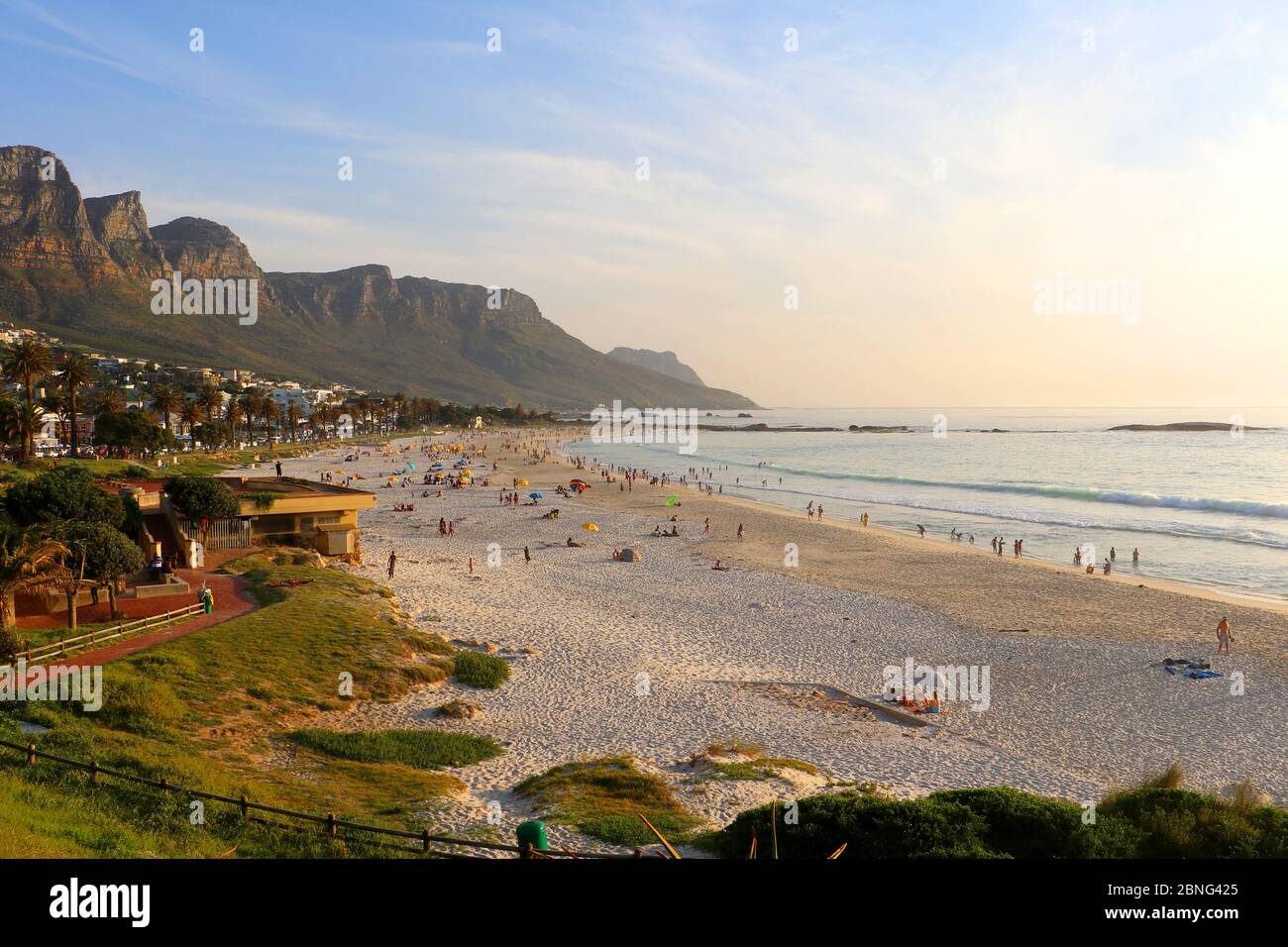 Proprietà e spiagge a Camps Bay, Città del Capo, Sud Africa in una giornata estiva limpida, con persone sulla spiaggia e le montagne sullo sfondo Foto Stock