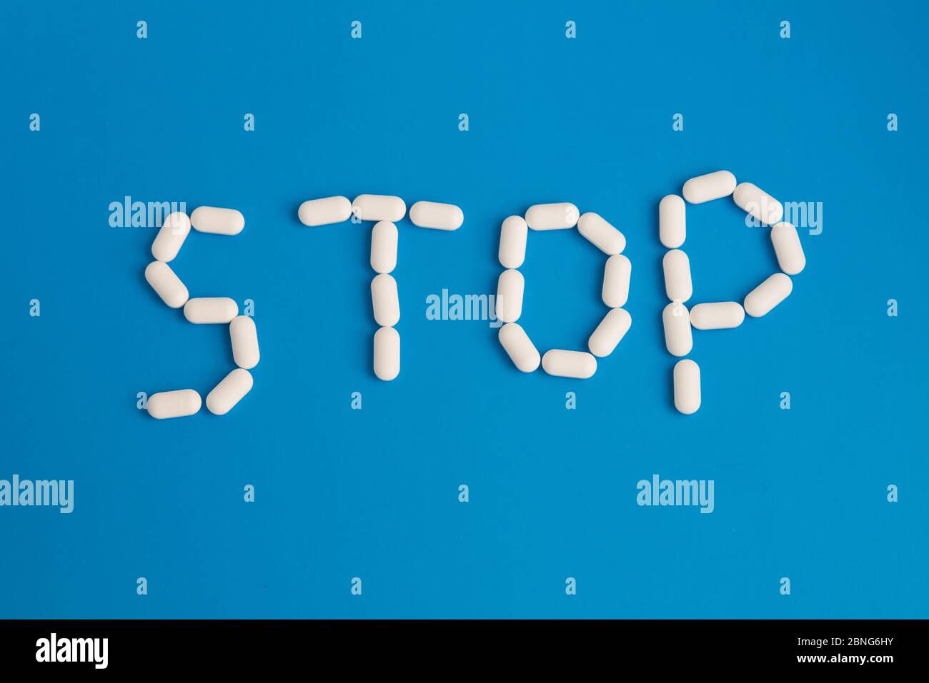 Piatto di stop parola fatta di pillole bianche su sfondo blu Foto Stock