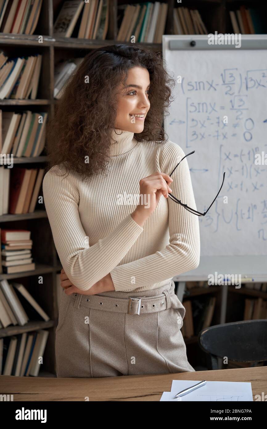 Felice sicuro insegnante ispanica giovane donna che guarda via sognando in classe. Foto Stock