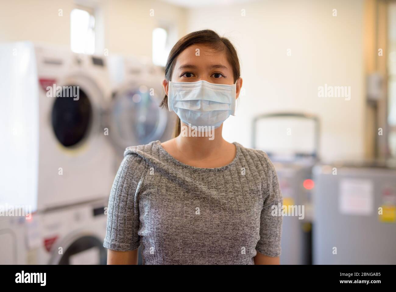 Giovane donna asiatica che indossa la maschera alla lavanderia automatica per la protezione da focolai di virus corona Foto Stock