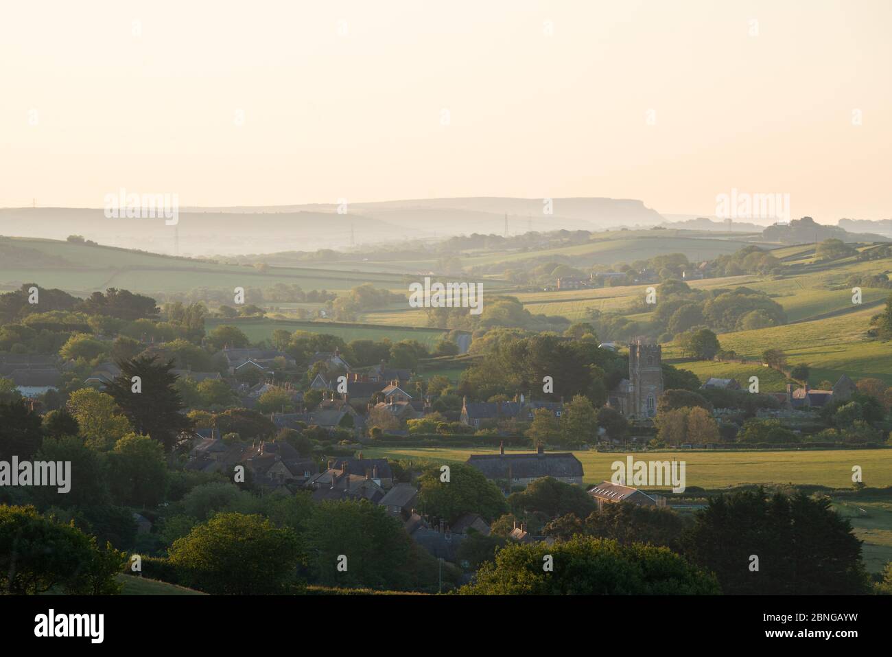 Abbotsbury, Dorset, Regno Unito. 15 MAGGIO 2020. Regno Unito Meteo. Alba fresca e chiara. Abbotsbury villaggio cattura i primi raggi di luce solare sulla costa meridionale del Dorset. Credit: Dan Tucker/Alamy Live Foto Stock