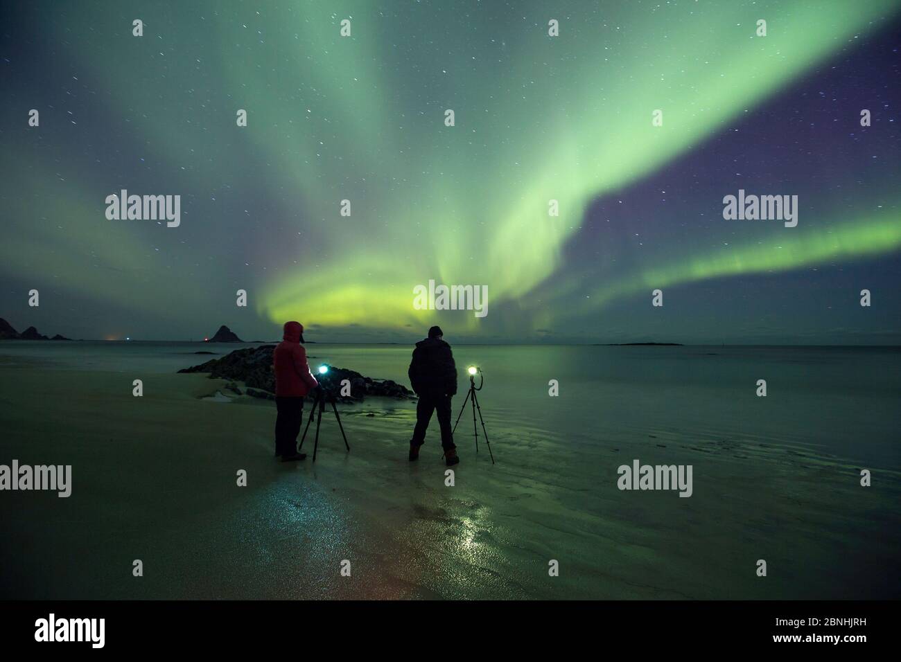 Persone che fotografano l'aurora boreale sulla spiaggia vicino all'isola degli uccelli Bleiksoya vicino ad Andenes, l'isola di Andoya, l'Oceano Atlantico del Nord, Norvegia, gennaio 20 Foto Stock