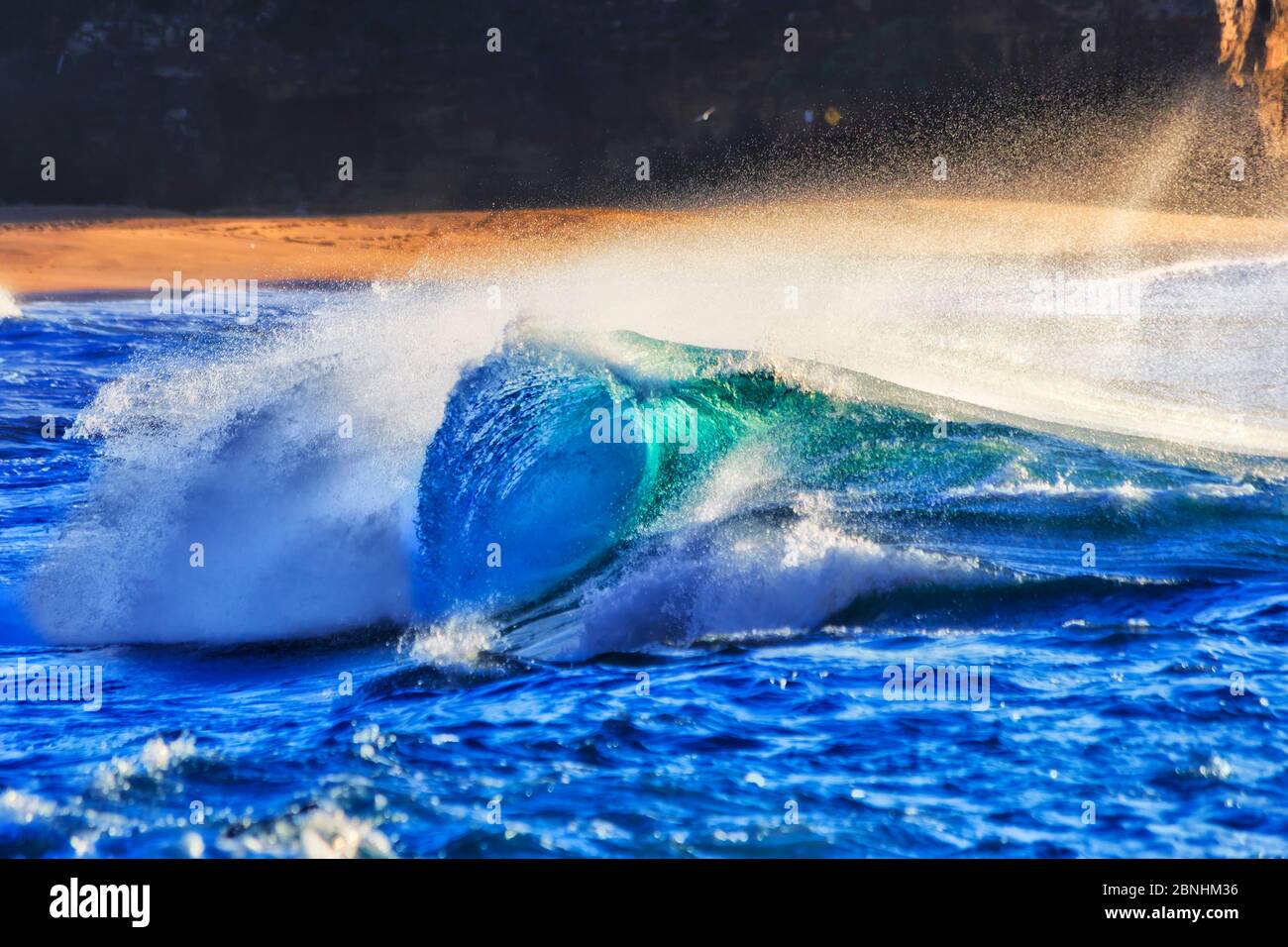 Una potente e veloce onda che si avvolgono nella luce del sole sulla spiaggia di Turimetta di Sydney contro il buio promontorio all'alba. Foto Stock