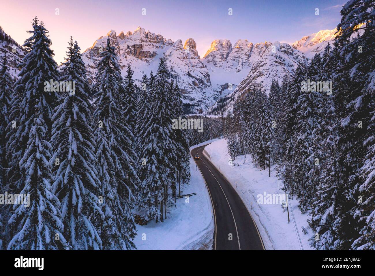 Veduta aerea con drone di auto viaggiando sulla strada panoramica Dobbiaco-Misurina lungo boschi innevati all'alba, Dolomiti, Alto Adige, Italia, Europa Foto Stock