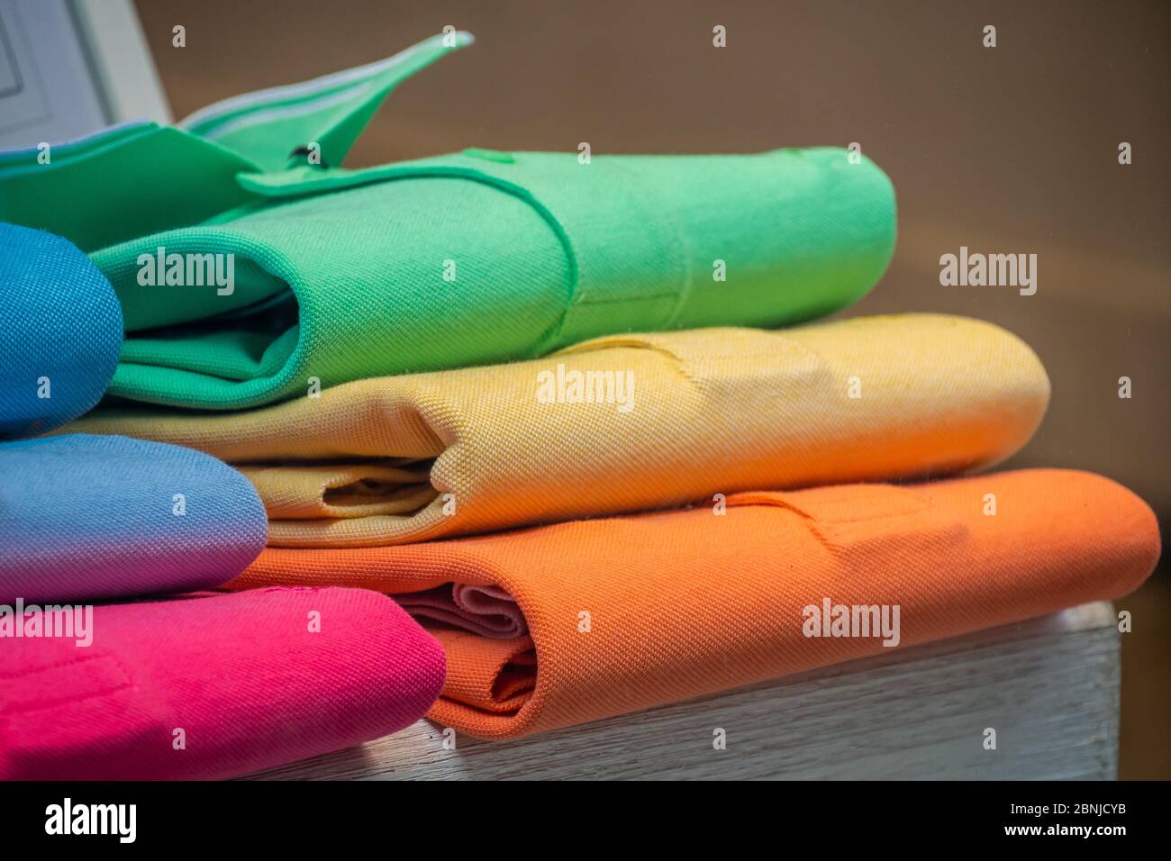 Un mucchio di camicie di polo in cotone in molti colori diversi, esposto in una vetrina. Foto Stock