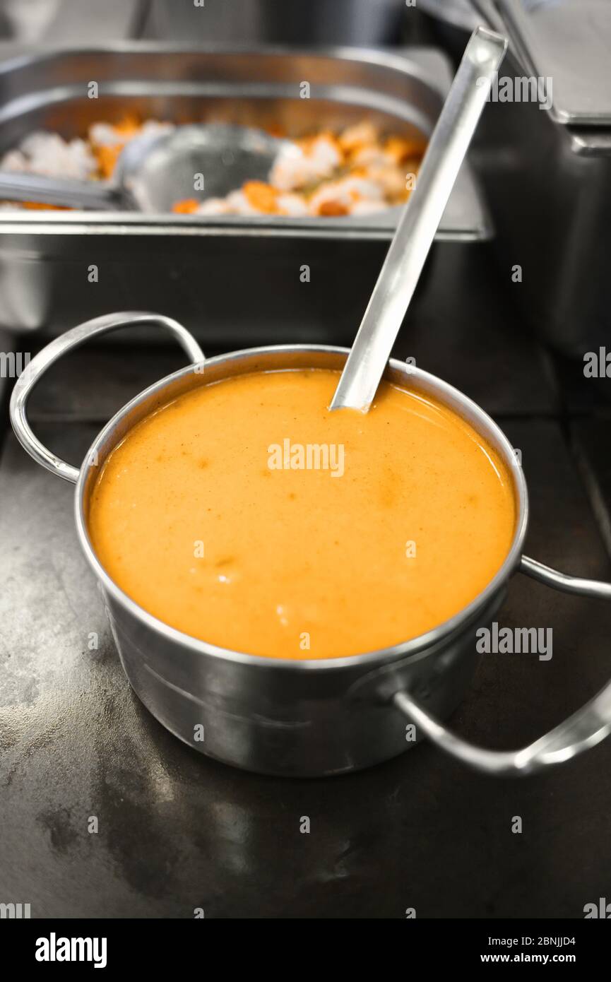 Zuppa gialla in un recipiente di metallo. Preparazione del pranzo nella sala da pranzo. Stufato esotico. Cibo in una piastra di acciaio. Foto Stock