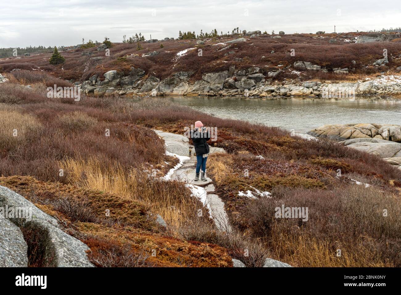 Una donna in un cappotto invernale scatta una foto della costa rocciosa della Nuova Scozia, Canada. Foto Stock