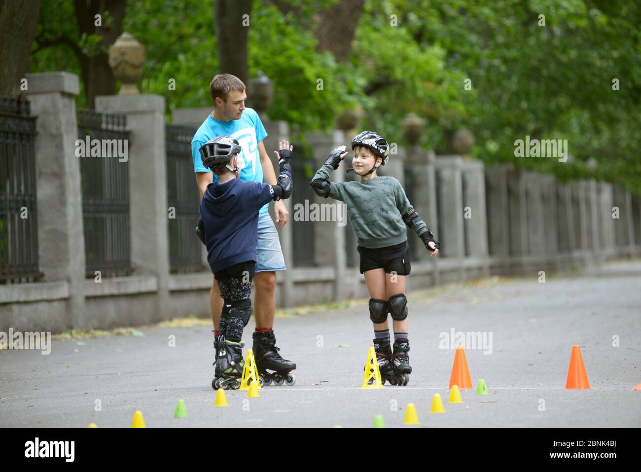 Rollerblading. Allenatore uomo che si aggira con i ragazzi in un parco Foto Stock