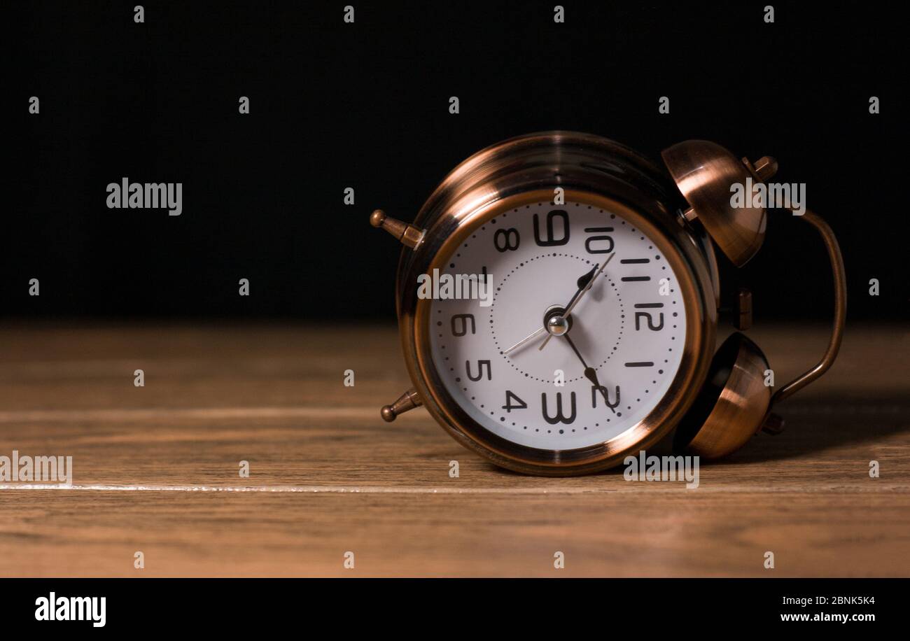 Antico orologio di allarme analogia metallo acciaio caduto lateralmente in un tavolo di legno con sfondo nero Foto Stock