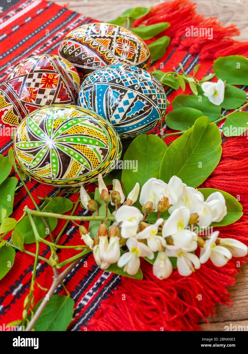 uova di pasqua rumene ortodosse decorate a mano con motivi tradizionali su un panno rosso con fiori di acacia da parte Foto Stock