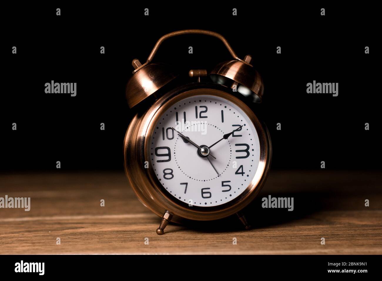 Sveglia vintage con primo piano in metallo color marrone campanello con tavolo in legno a mezzanotte e sfondo nero Foto Stock