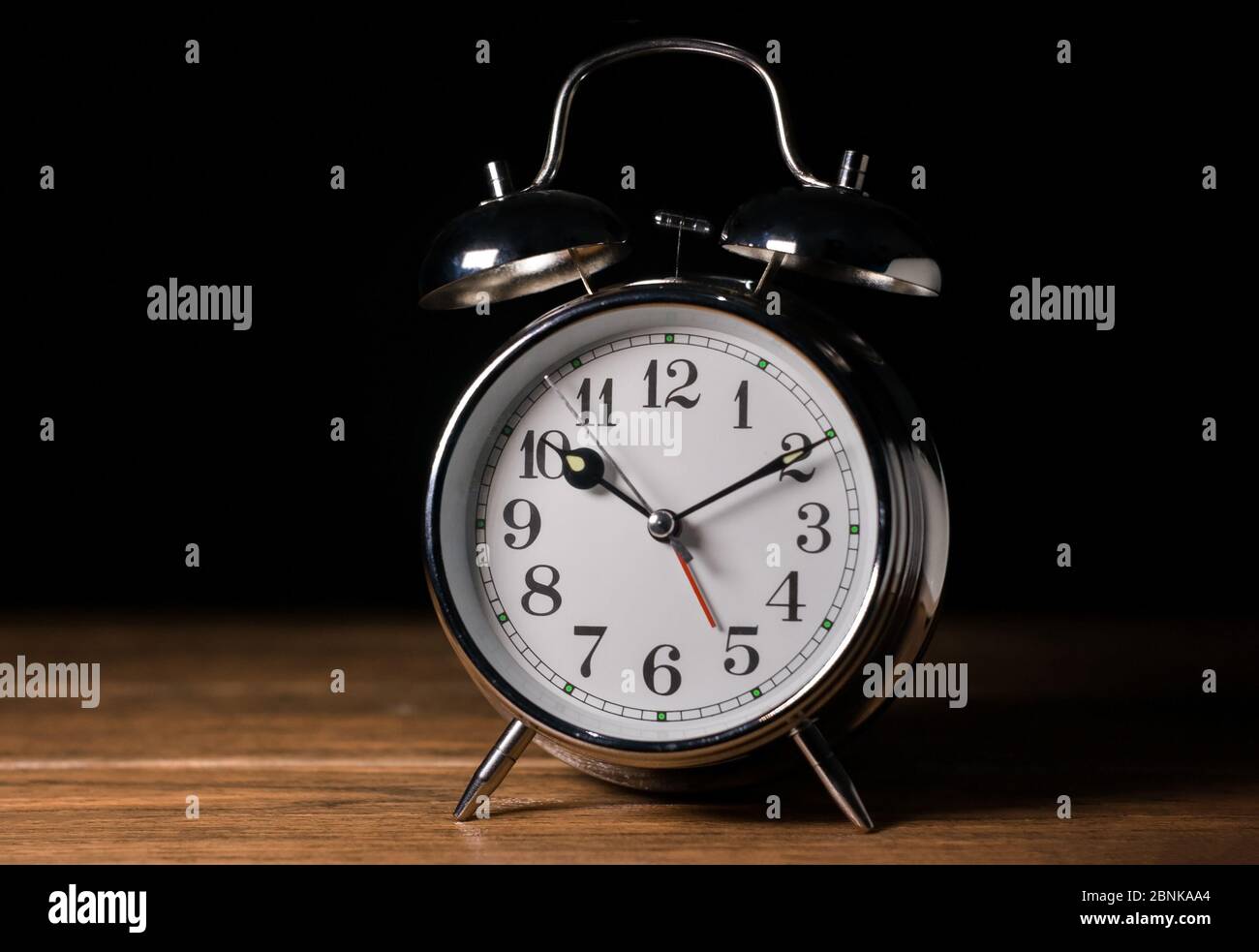 Una sveglia con campana classica metallizzata a mezzanotte con tavolo in legno e sfondo nero scuro Foto Stock