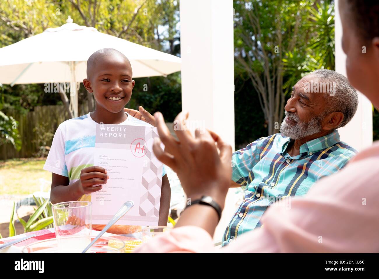 Ragazzo afroamericano che mostra al nonno i suoi compiti durante un pranzo di famiglia in giardino Foto Stock