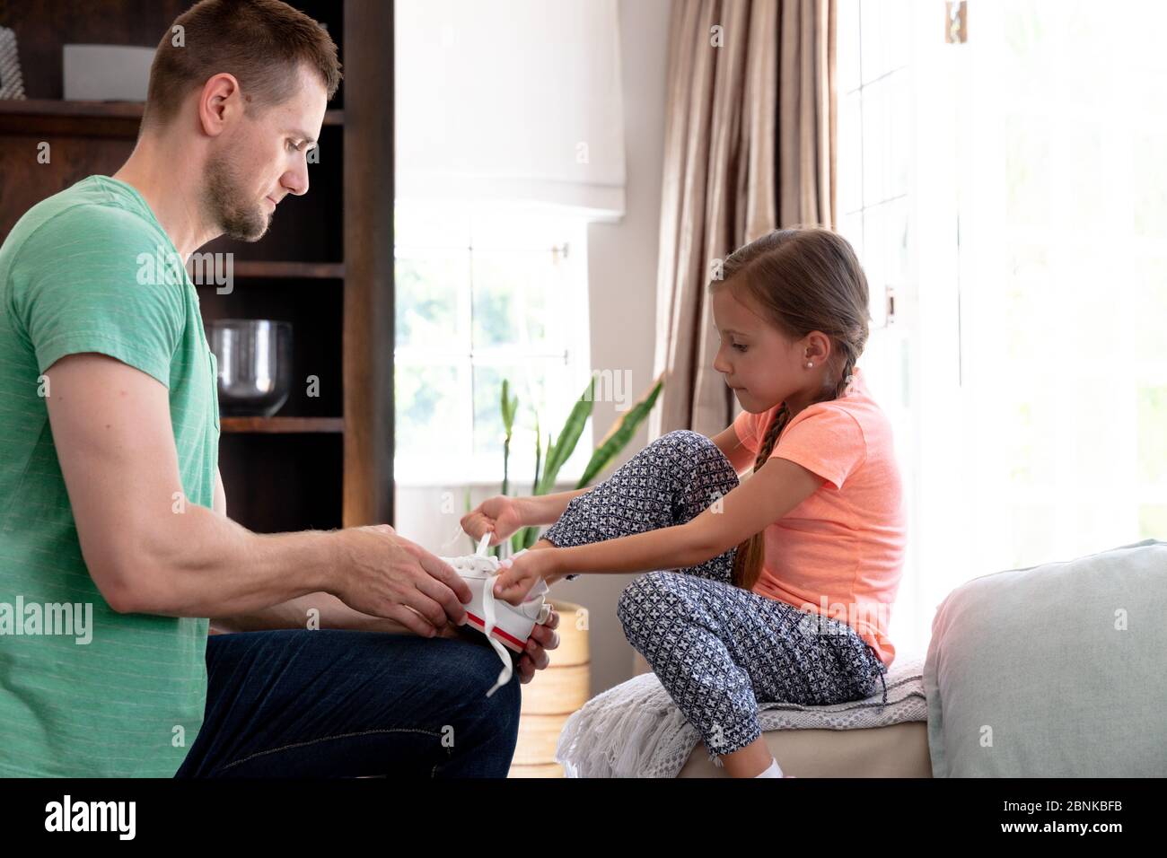 Caucasica ragazza seduta su un divano mentre suo padre sta aiutandola a mettere sulle scarpe Foto Stock