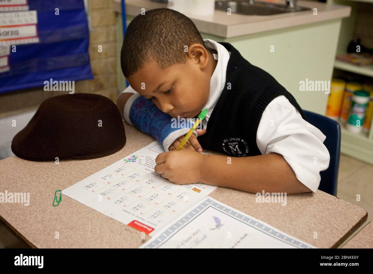 Austin Texas USA, gennaio 2013: Il ragazzo nero di seconda classe che indossa una divisa usa una matita con gomma verde alla fine per completare un foglio di lavoro nella sua classe in una scuola privata cattolica. ©Bob Daemmrich Foto Stock