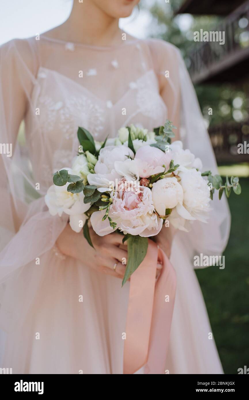 Primo piano bouquet sposa, il bouquet è composto da peonie bianche e rosa, eucalipto. La sposa vestita con abito da sposa rosa tiene il bouquet Foto Stock
