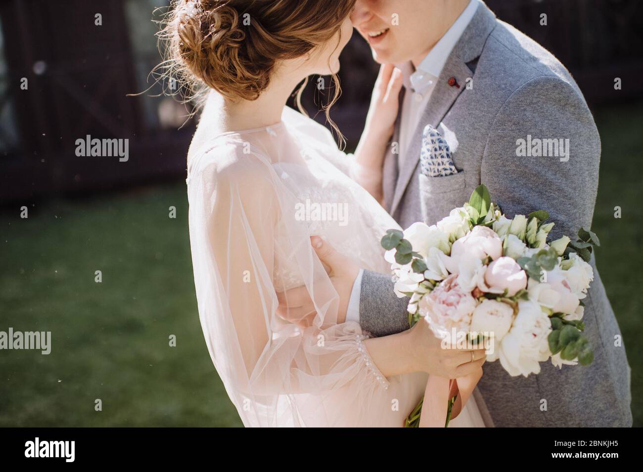 L'abbraccio dello sposo e della sposa, si levano in piedi l'uno di fronte all'altro. La sposa in un abito rosa tiene in mano un bouquet di peonie bianche e rosa. Il bouquet è cravatta Foto Stock
