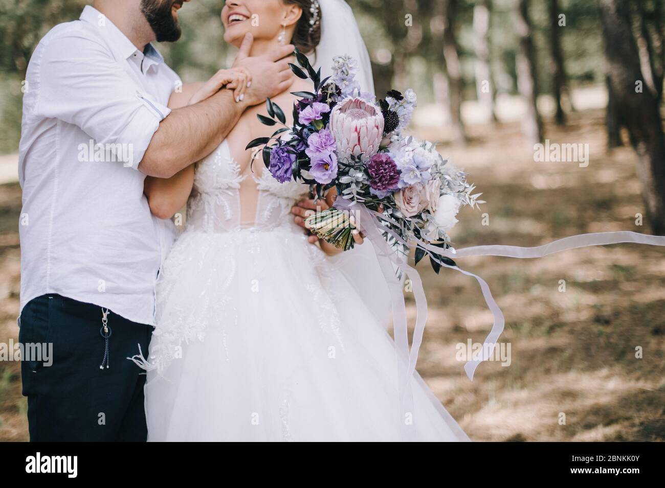 Primo piano del bouquet di rose, garofani, protei e foglie d’argento di una sposa nei toni del bianco, rosa, viola e lavanda. La sposa in un abito bianco pizzo Foto Stock